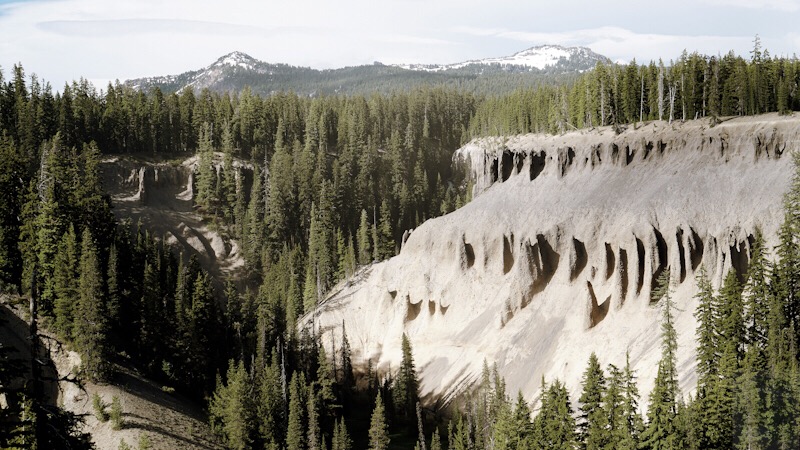 Crater Lake view with evergreen trees and sandy colored cliffs